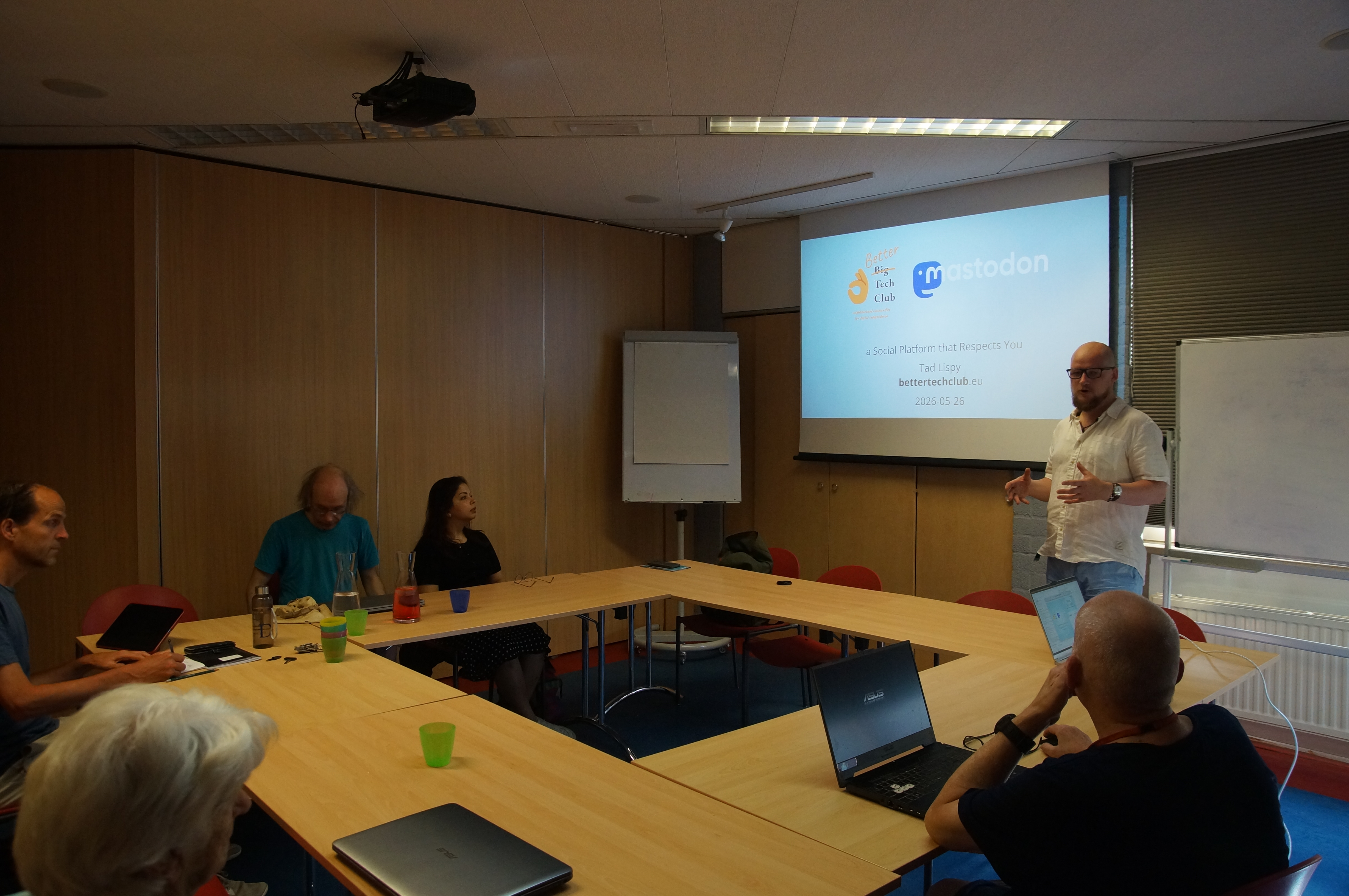 Presentation in the library. The speaker stands in front of a projector screen with the title slide, and logos of the Better Tech Club and Mastodon